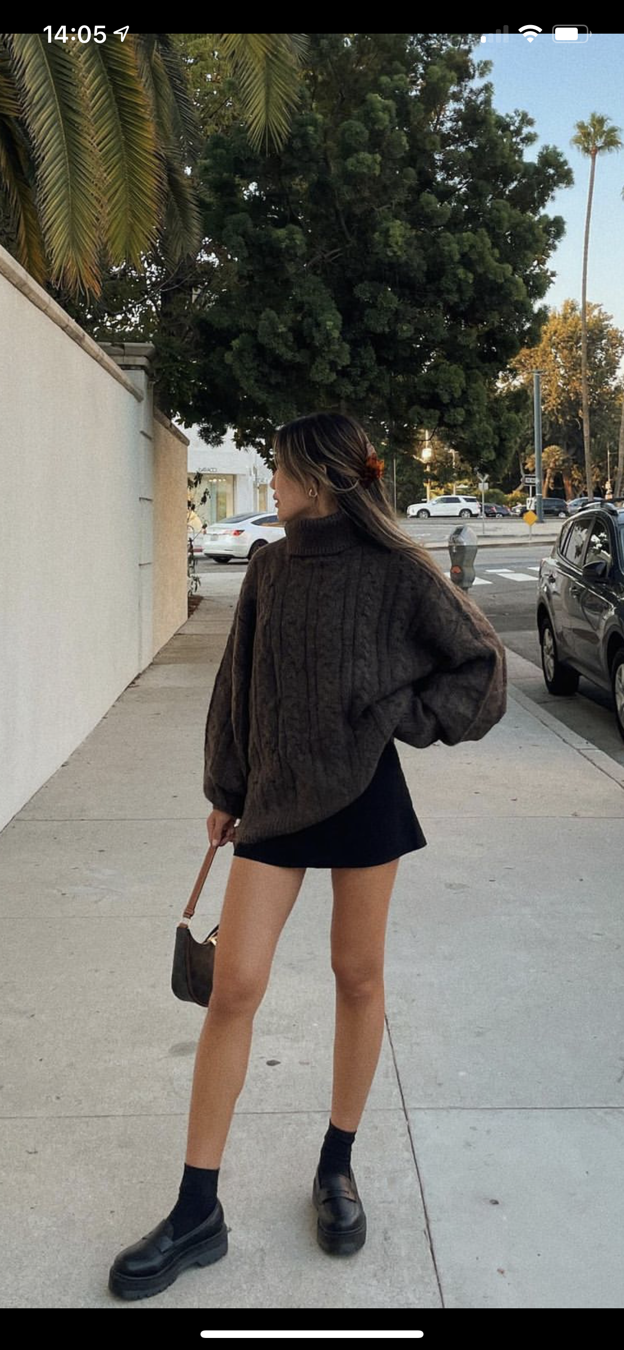 Gros pull beige avec mini jupe à volants blanche sur fond urbain.