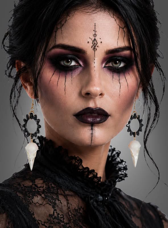 Femme avec maquillage sombre et détails graphiques noirs, portant des boucles d'oreilles blanches et noires.